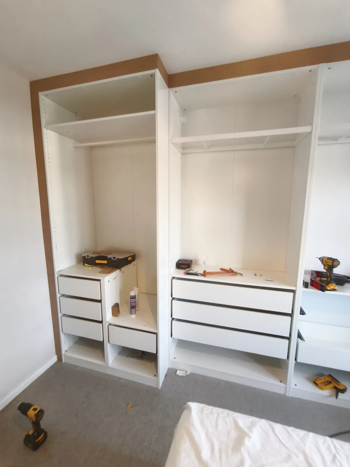 IKEA PAX frames fixed to the wall before the doors go on, with filler boards closing the gap above the units